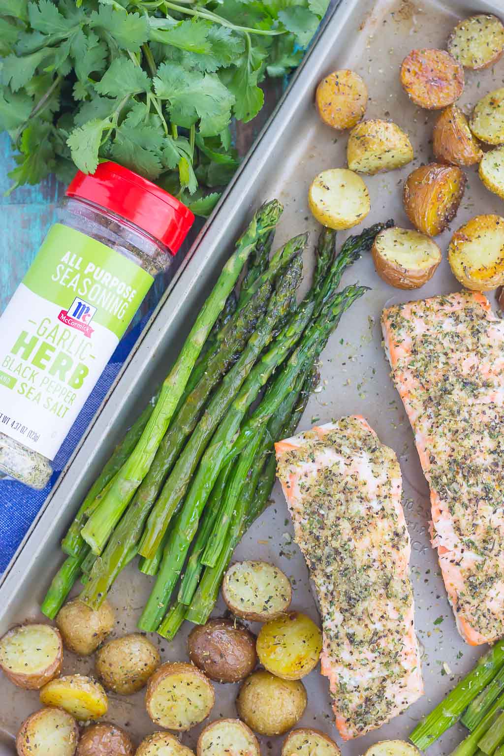 overhead view of a salmon sheet pan dinner next to jar of seasoning and fresh cilantro 