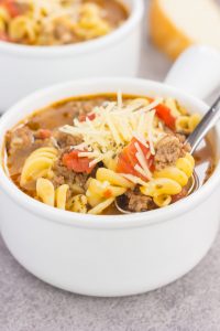 a spoon digging into a white bowl of one pot lasagna soup