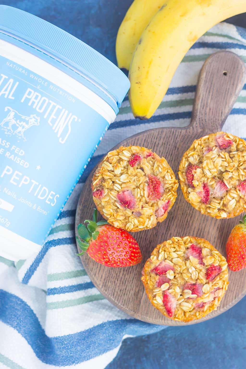 Overhead view of three strawberry baked oatmeal cups on a wood board next to a container of collagen. 