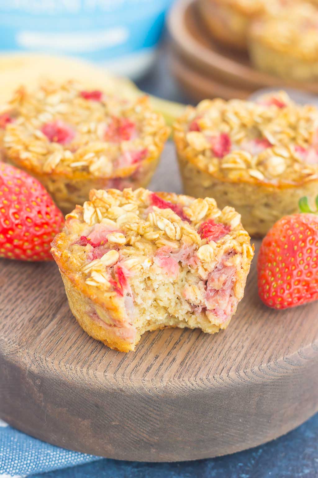 Three strawberry banana oatmeal cups on a wood platter. The front oatmeal cup has a bite missing. 