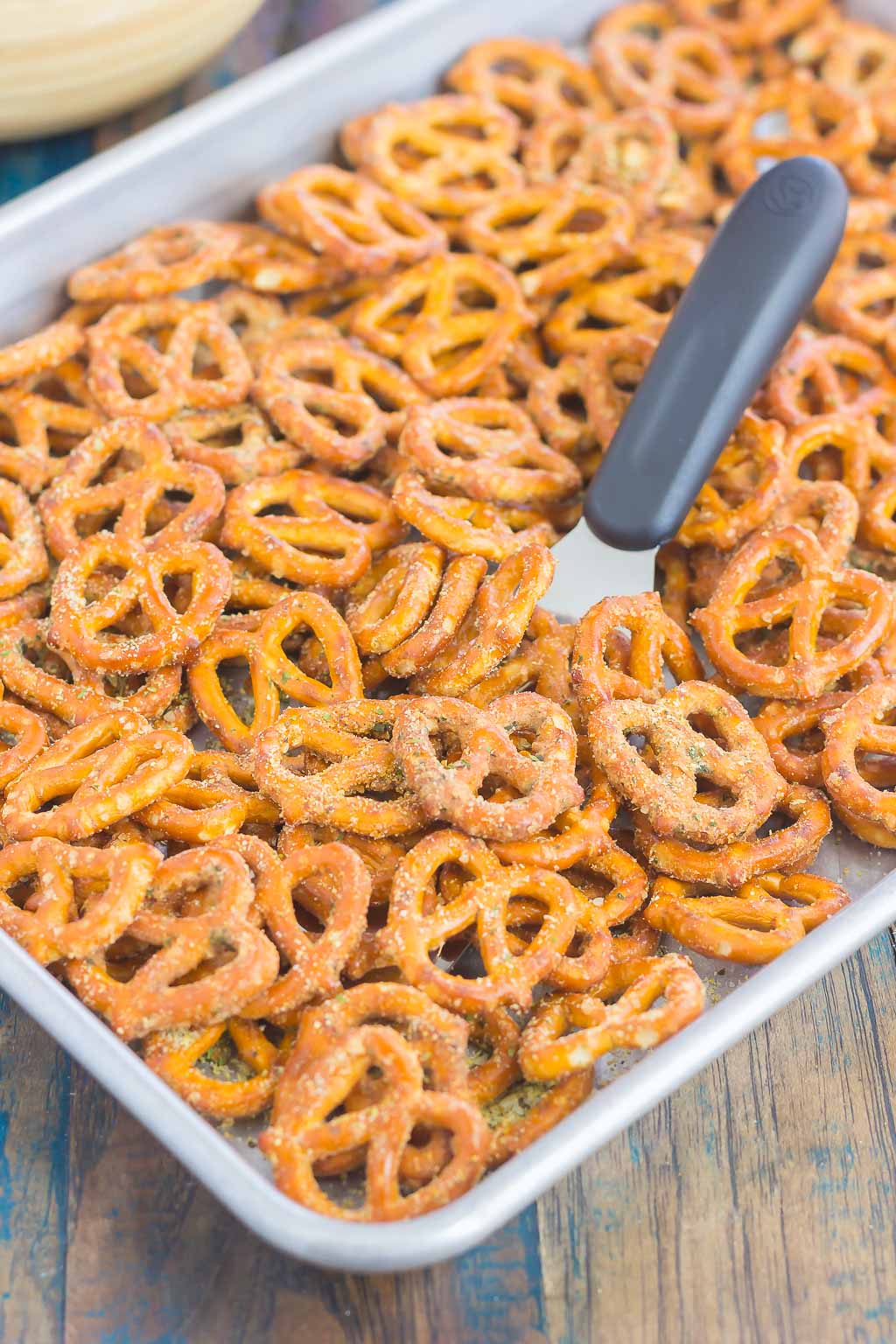 ranch seasoned pretzels on a baking tray. A small spatula pokes out of the center. 