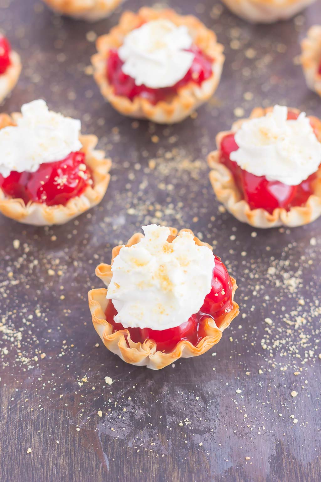 mini cherry pie bites topped with whipped cream on a gray surface. 