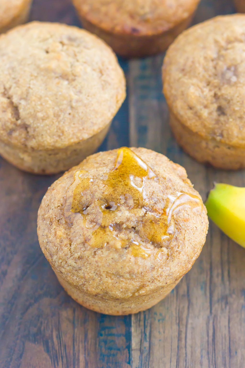 Top view of three whole wheat banana muffins. One has been drizzled with honey. 