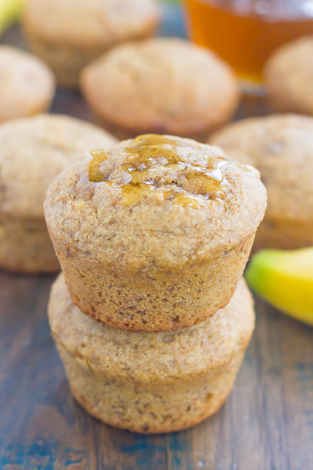 Two whole wheat banana muffins stacked on top of each other. More muffins are in the background. 