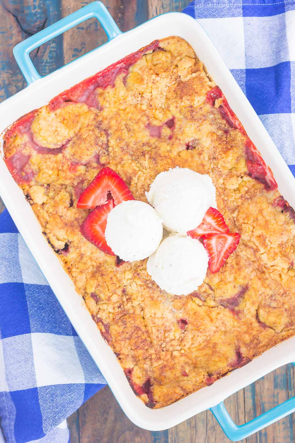 A baking dish of strawberry dump cake, garnished with strawberries and vanilla ice cream. 