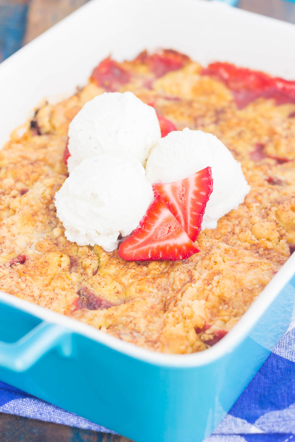 A baking dish of strawberry dump cake, garnished with strawberries and vanilla ice cream. 