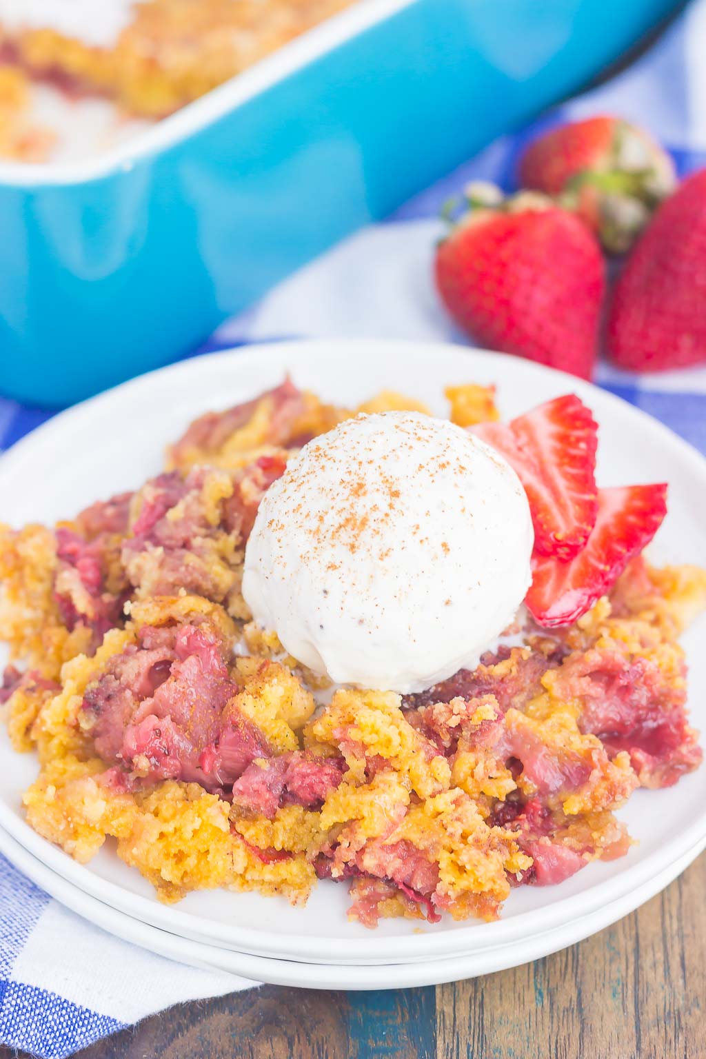 A serving of dump cake with strawberries and vanilla ice cream on a white dessert plate. 