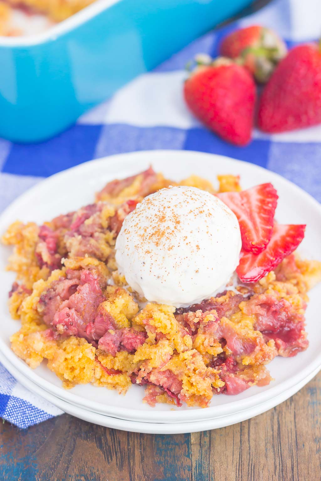 A serving of dump cake with strawberries and vanilla ice cream on a white dessert plate. 