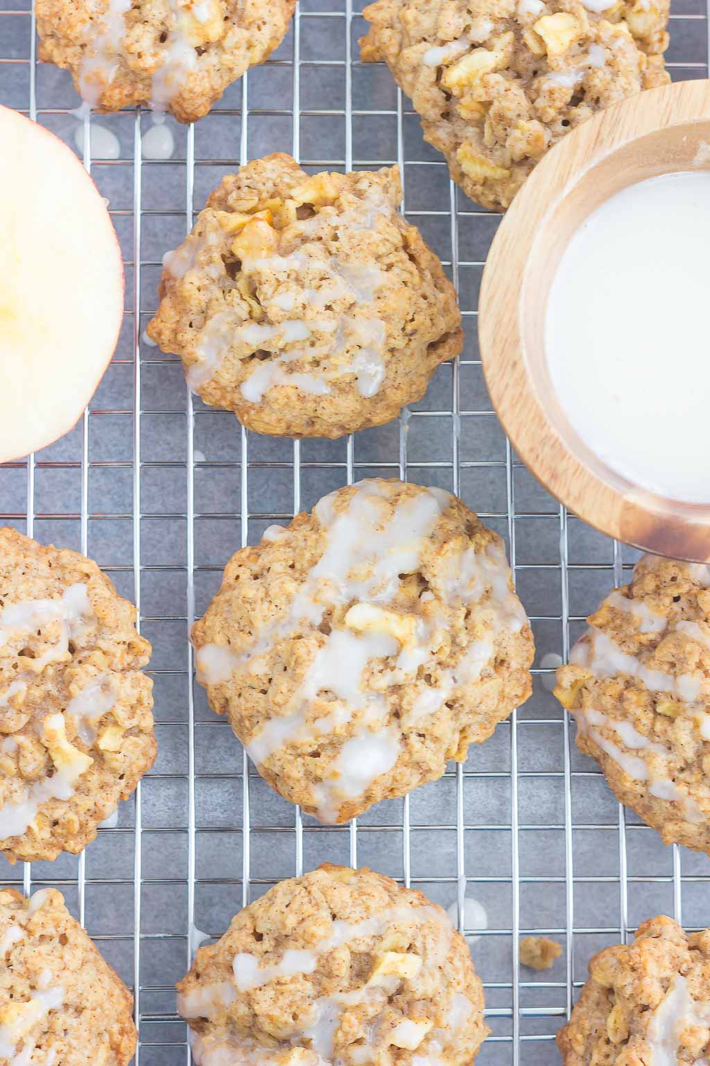 overhead view of apple cookies cooling on a wire rack. A bowl of glaze rests on the side. 