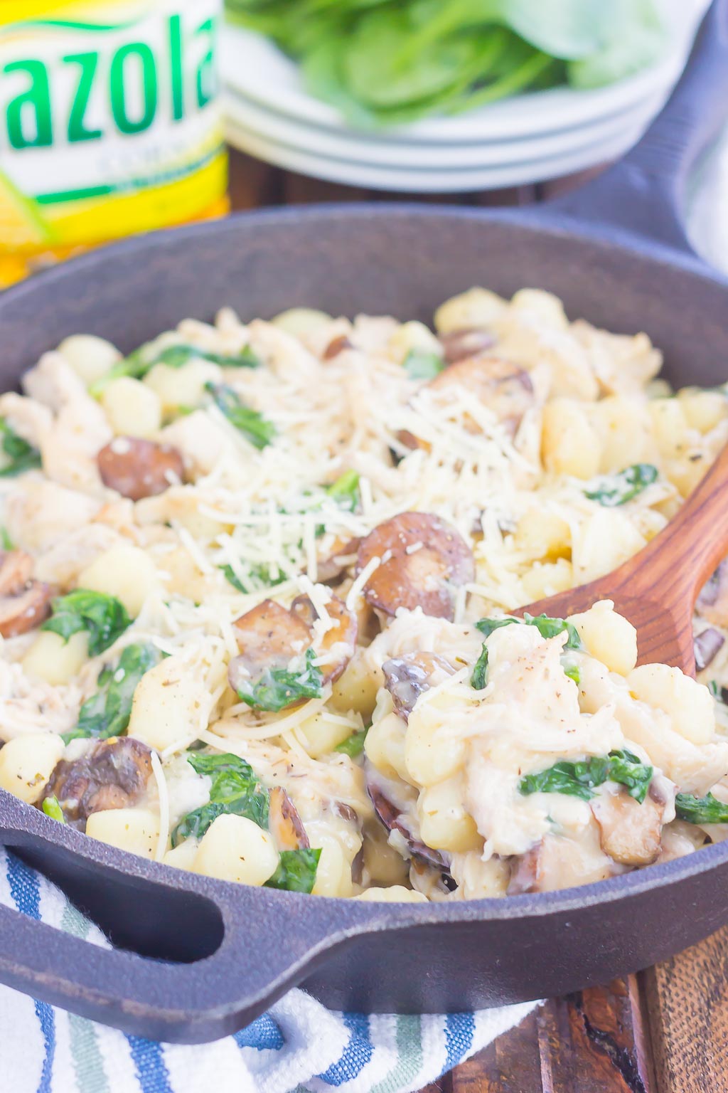 spinach and chicken gnocchi pasta in a cast iron skillet. A wooden spoon is scooping out a portion. 