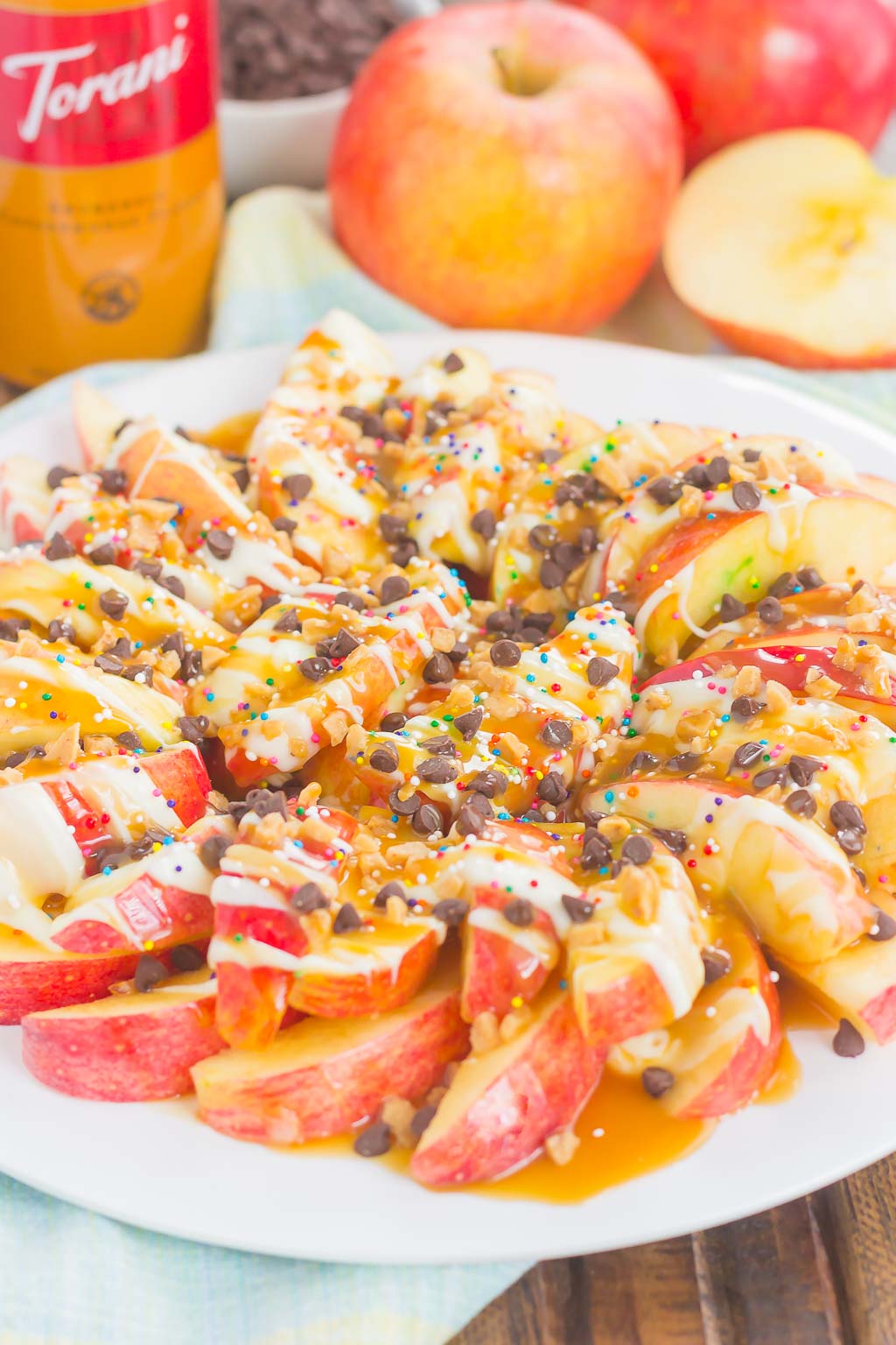 These Caramel Apple Nachos make a deliciously easy snack that's perfect for just about any time. Apple slices are drizzled with a rich caramel sauce and white chocolate, and then topped with toffee bits, chocolate chips, and sprinkles. This simple treat is ready in less than 10 minutes and is sure to be a crowd-pleaser! #apples #applerecipe #caramelapple #nachos #applenachos #caramelapplenachos #appledessert #applesnack #falldessert #fallsnack