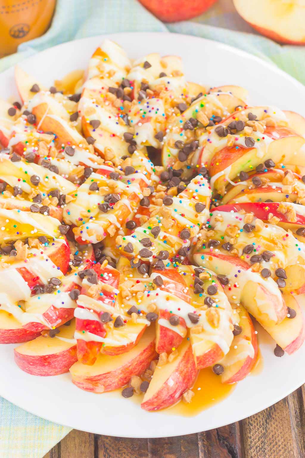 These Caramel Apple Nachos make a deliciously easy snack that's perfect for just about any time. Apple slices are drizzled with a rich caramel sauce and white chocolate, and then topped with toffee bits, chocolate chips, and sprinkles. This simple treat is ready in less than 10 minutes and is sure to be a crowd-pleaser! #apples #applerecipe #caramelapple #nachos #applenachos #caramelapplenachos #appledessert #applesnack #falldessert #fallsnack