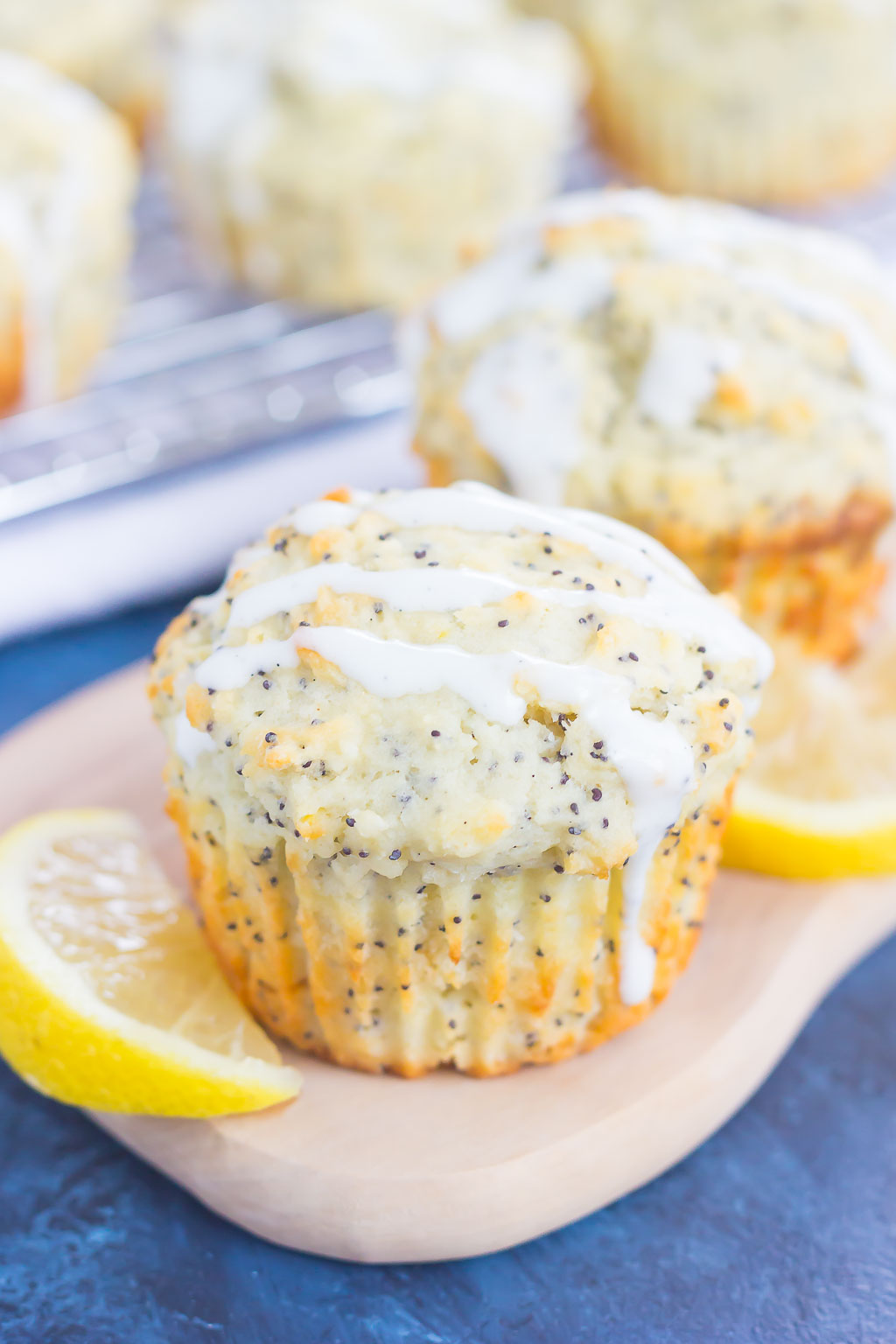 Two glazed lemon poppy seed muffins on a tray with lemon slices. 