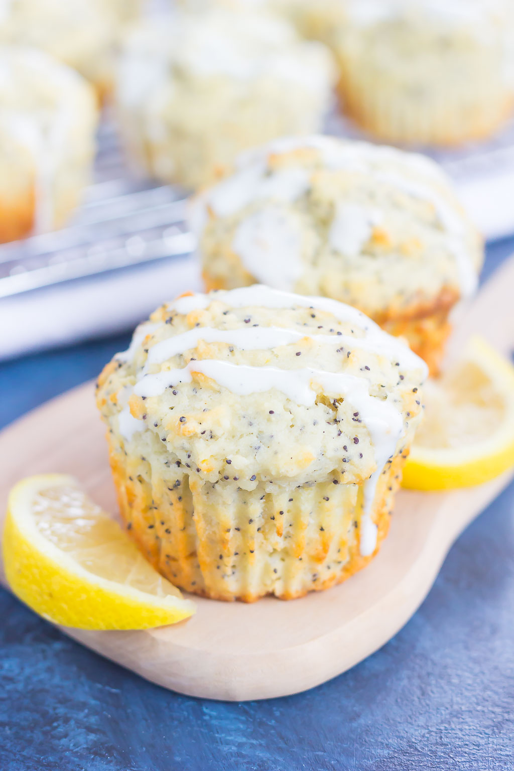 Two glazed lemon poppy seed muffins on a tray with lemon slices. 