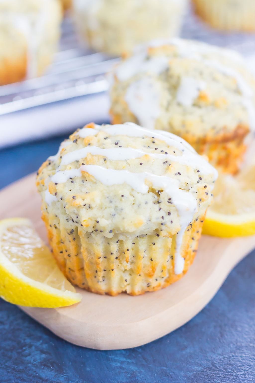 Two glazed lemon poppy seed muffins on a tray with lemon slices. 