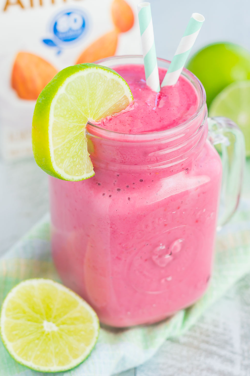 lime raspberry smoothie in mason jar garnished with lime wedge and two straws