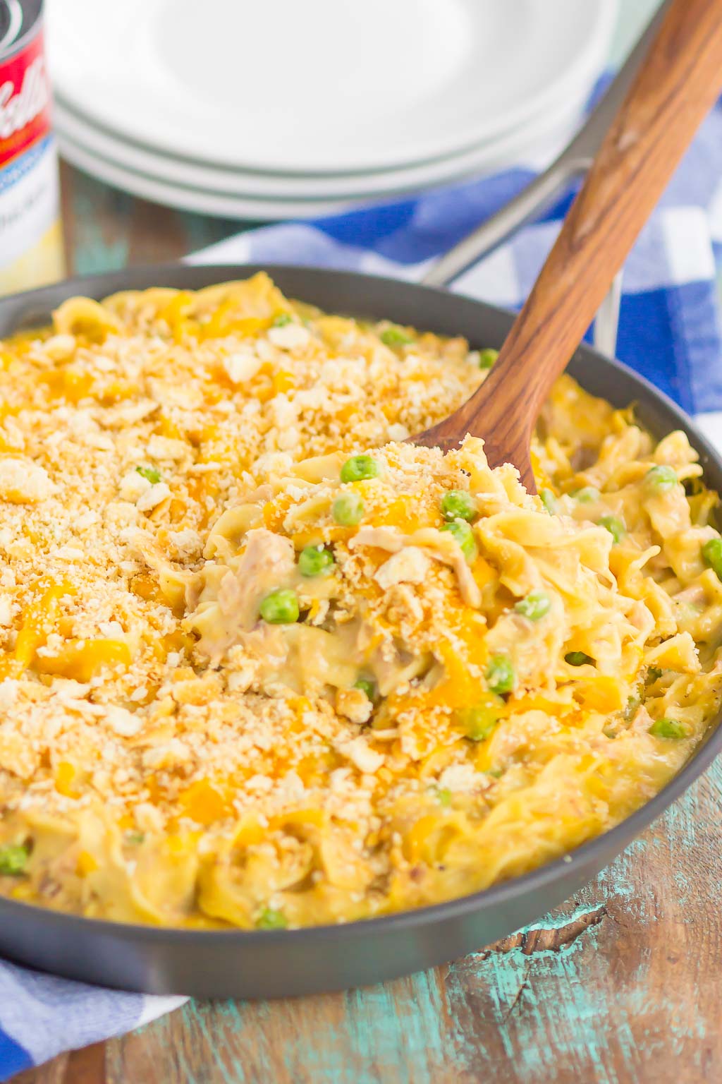 tuna noodle casserole with cheese in a large skillet with a wood spoon