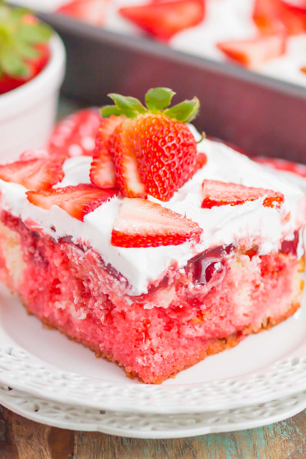 A slice of strawberry poke cake on a white dessert plate. 