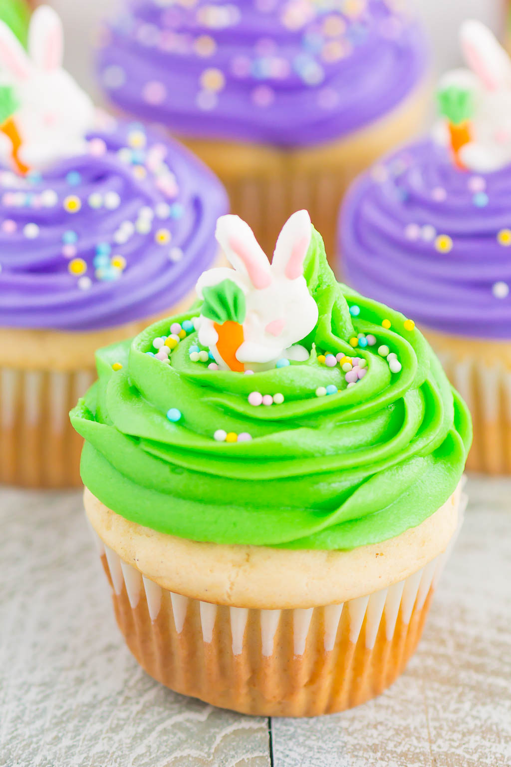 four Easter bunny cupcakes with brightly colored frosting and sprinkles 