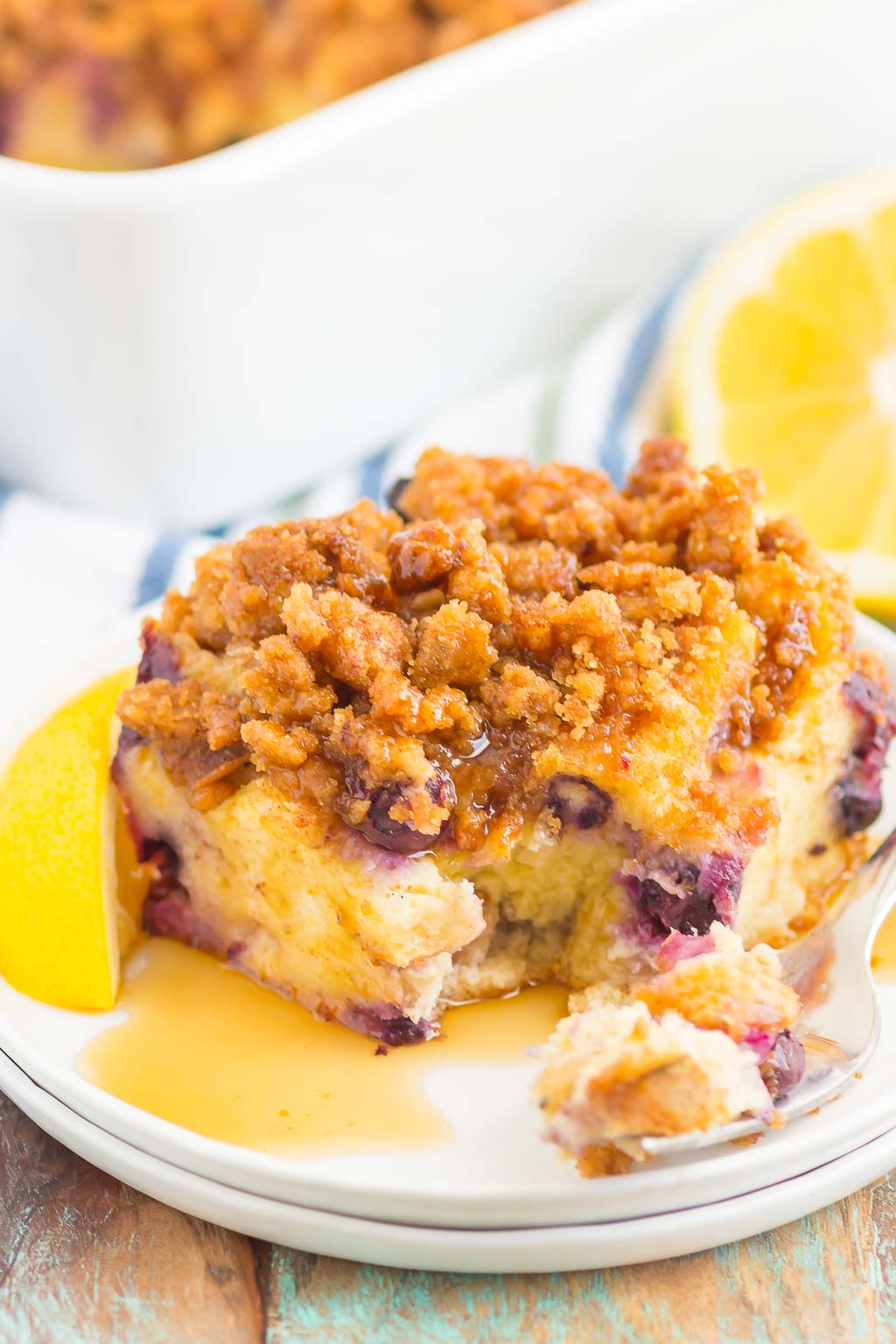 A slice of lemon blueberry french toast casserole on a white dessert plate. A fork also rests on the plate. 