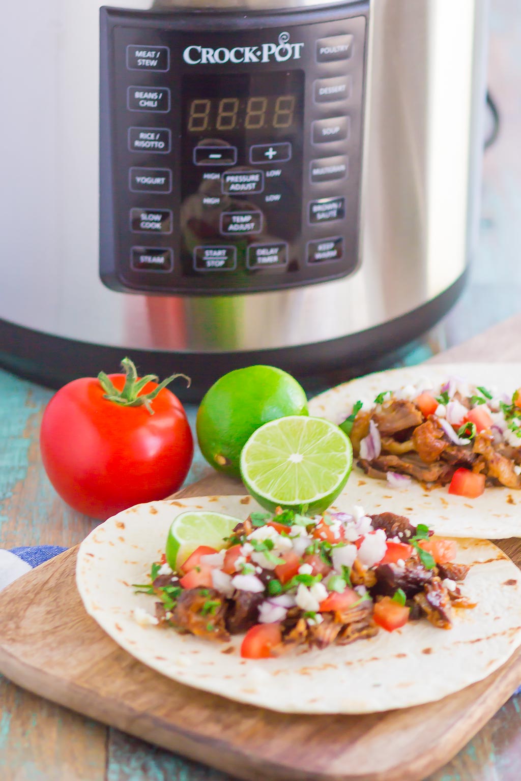 Two bbq pulled pork tacos on a cutting board. A CrockPot multi cooker is in the background. 