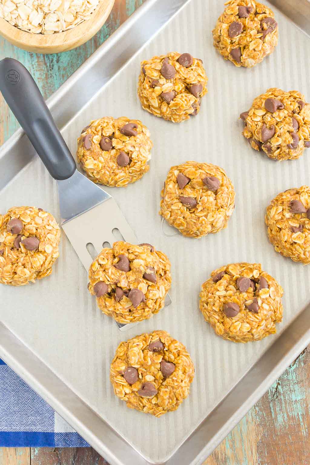 Overhead view of no bake almond butter oatmeal cookies on a baking sheet with a small spatula. 