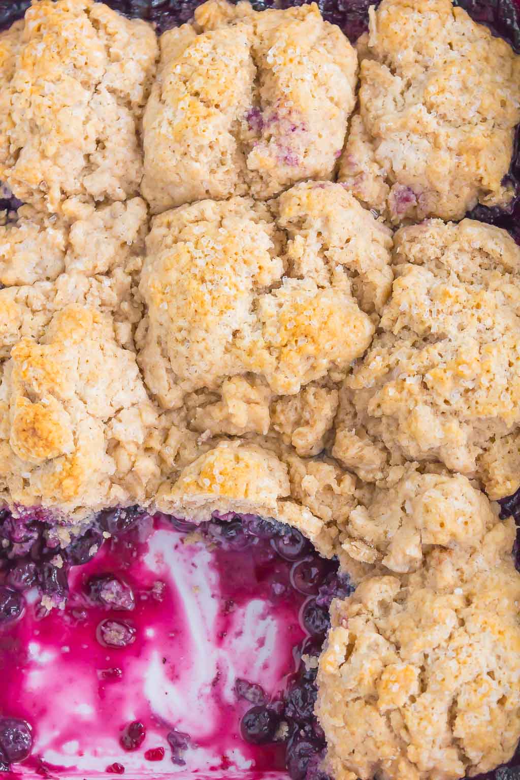 Overhead view of homemade blueberry cobbler in a baking dish. A serving has been spooned out already. 