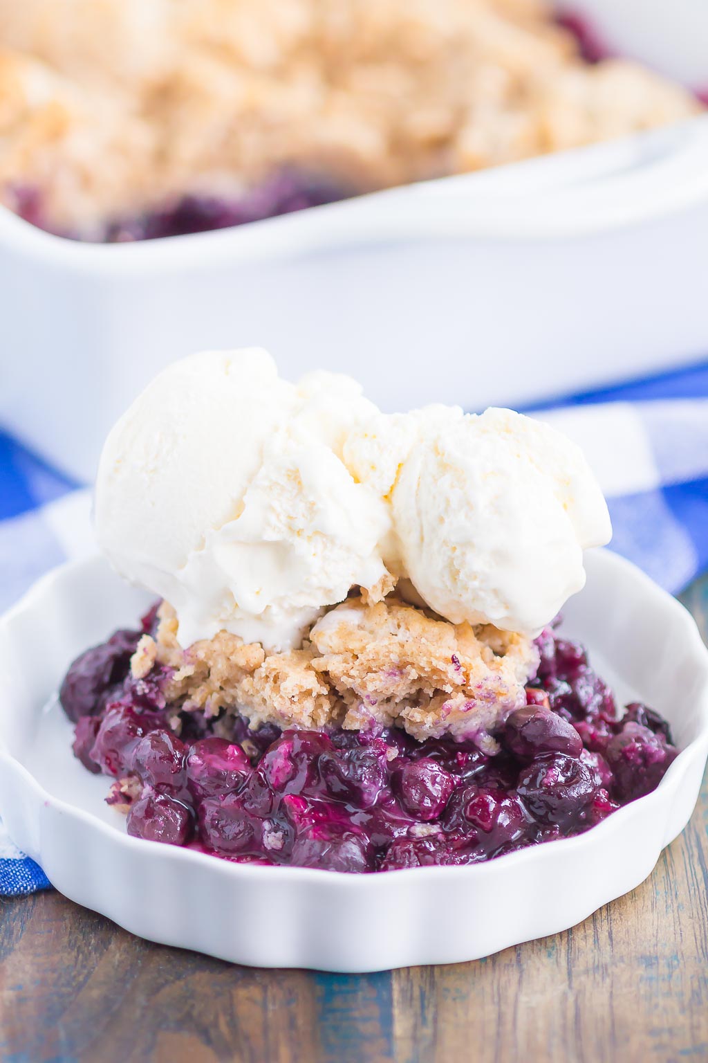 A helping of easy blueberry cobbler topped with vanilla ice cream in a white dish. 