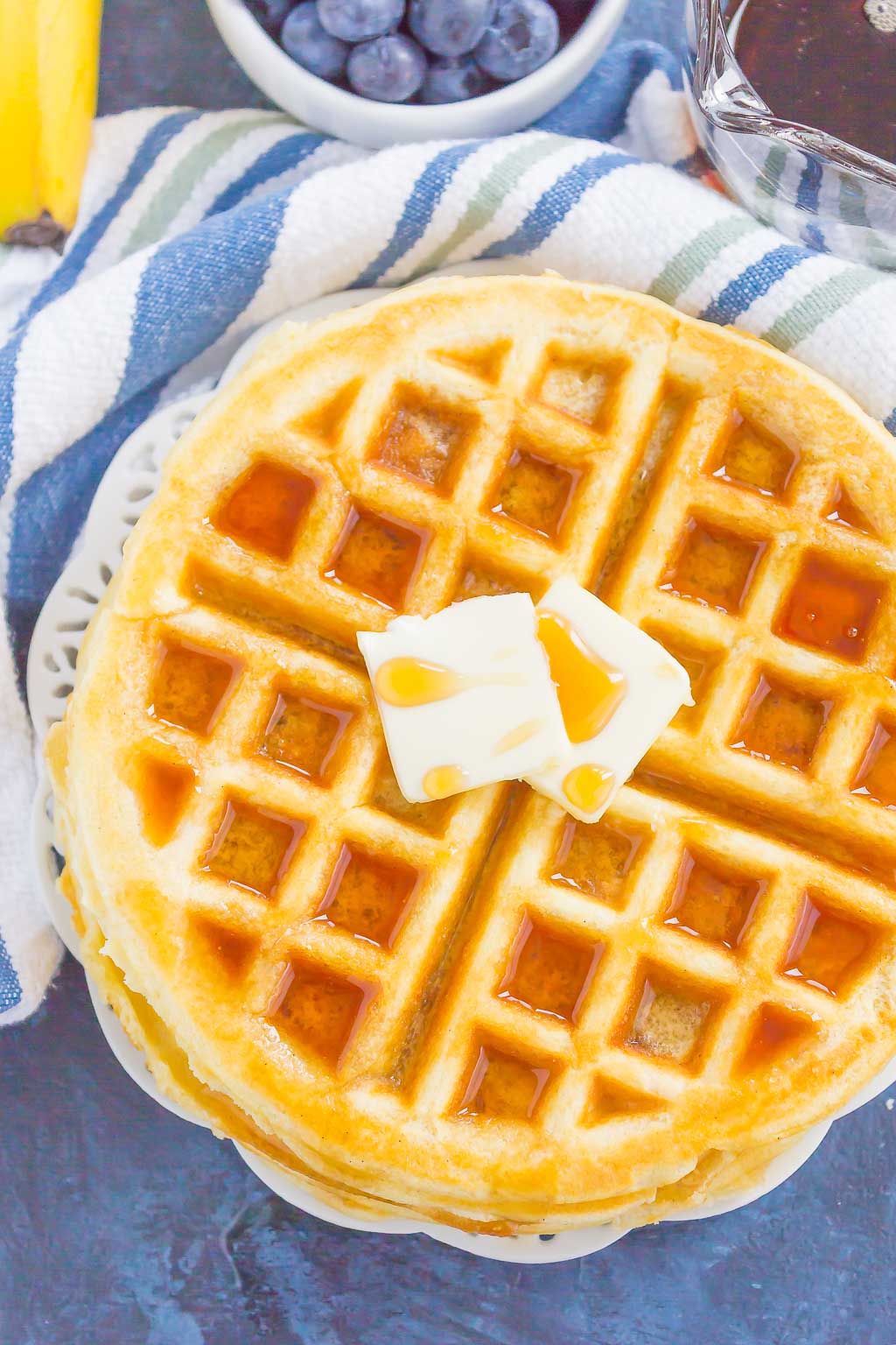 Overhead view of a stack of homemade waffles topped with syrup and butter. 