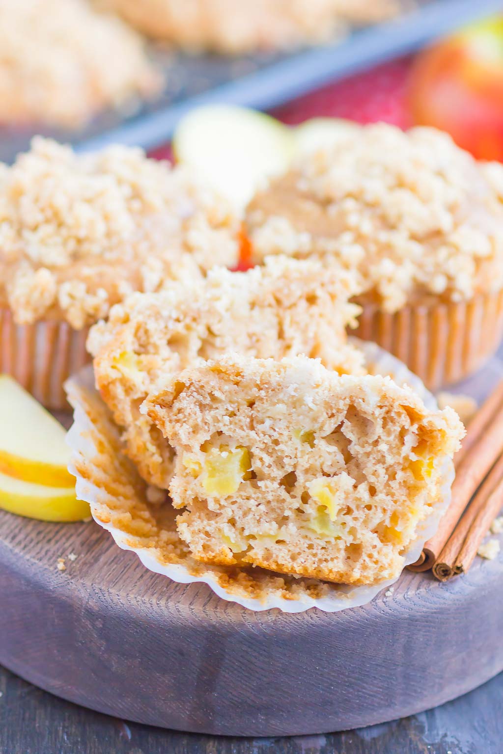 three apple crumble muffins on a wood serving tray. One muffin is cut in half. 