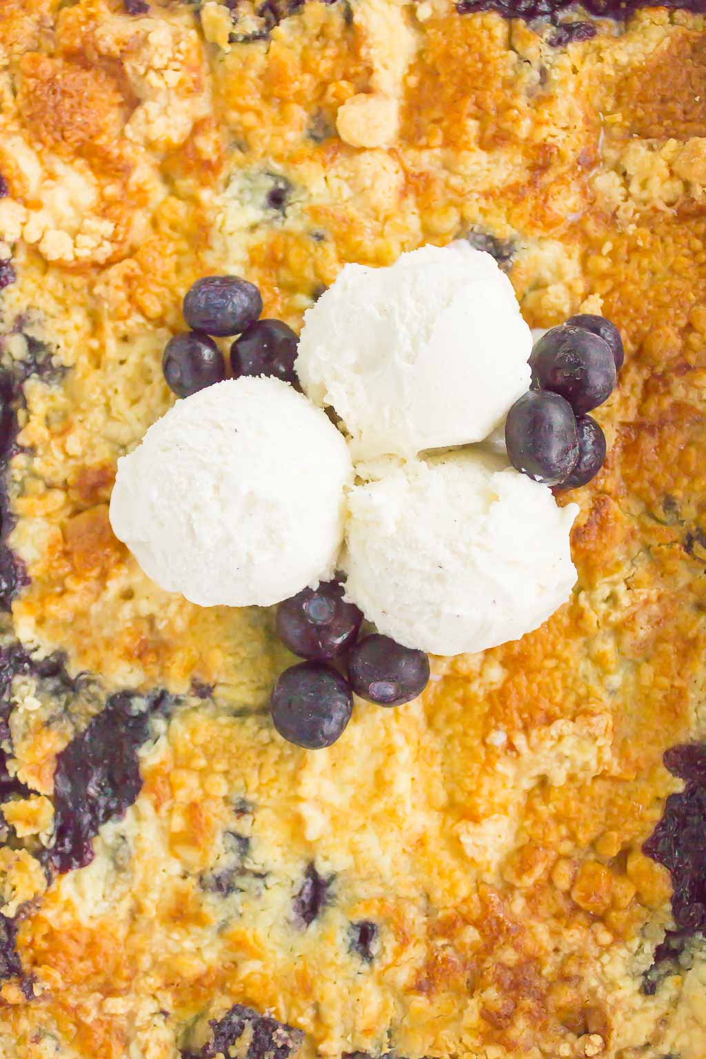 Overhead view of a blueberry dump cake made with frozen fruit. It's topped with three scoops of vanilla ice cream. 