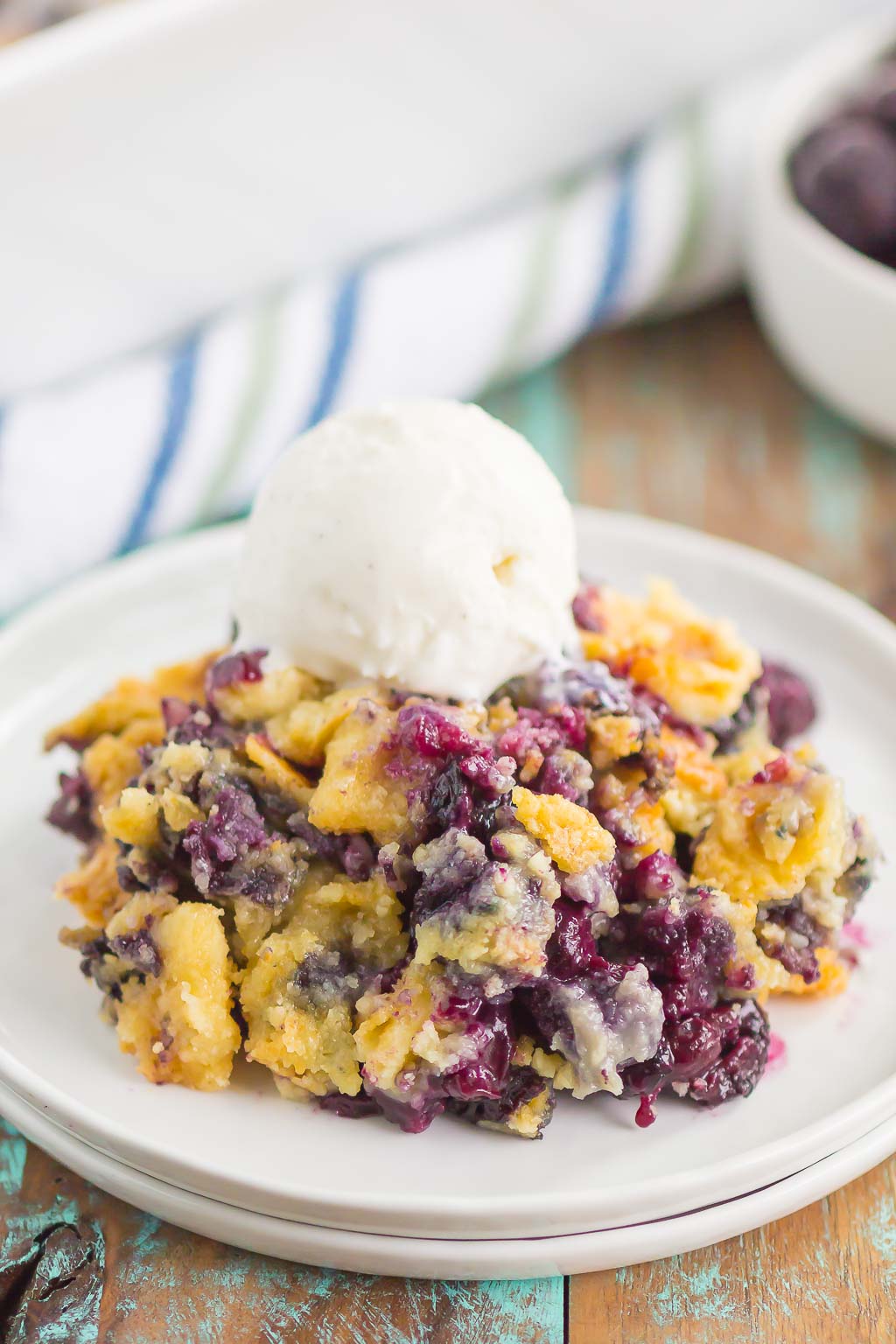 A serving of blueberry dump cake on a white plate, topped with ice cream. 