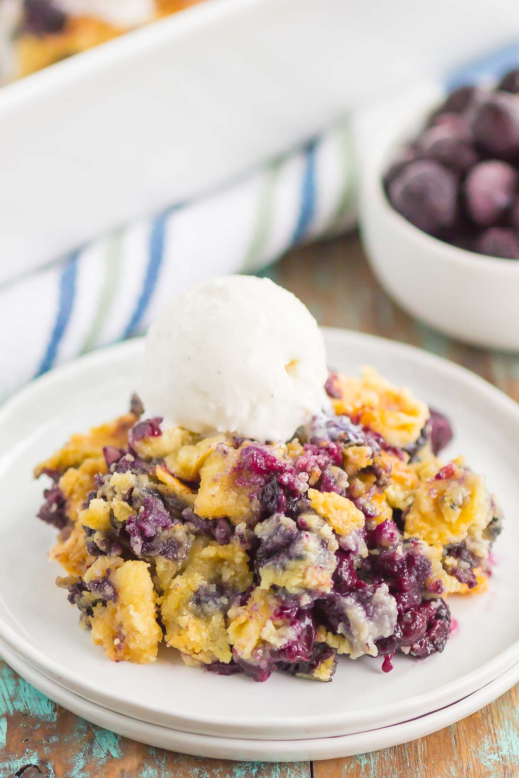 A serving of blueberry dump cake on a white plate, topped with ice cream. 