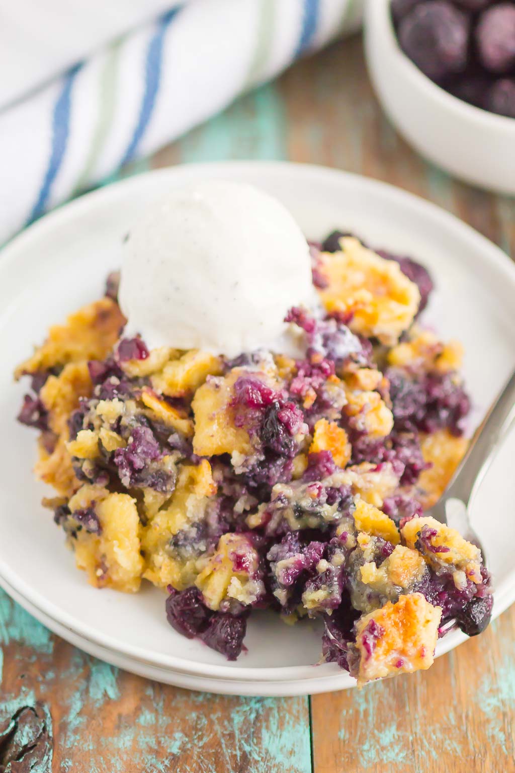 A serving of blueberry dump cake on a white plate, topped with ice cream. 