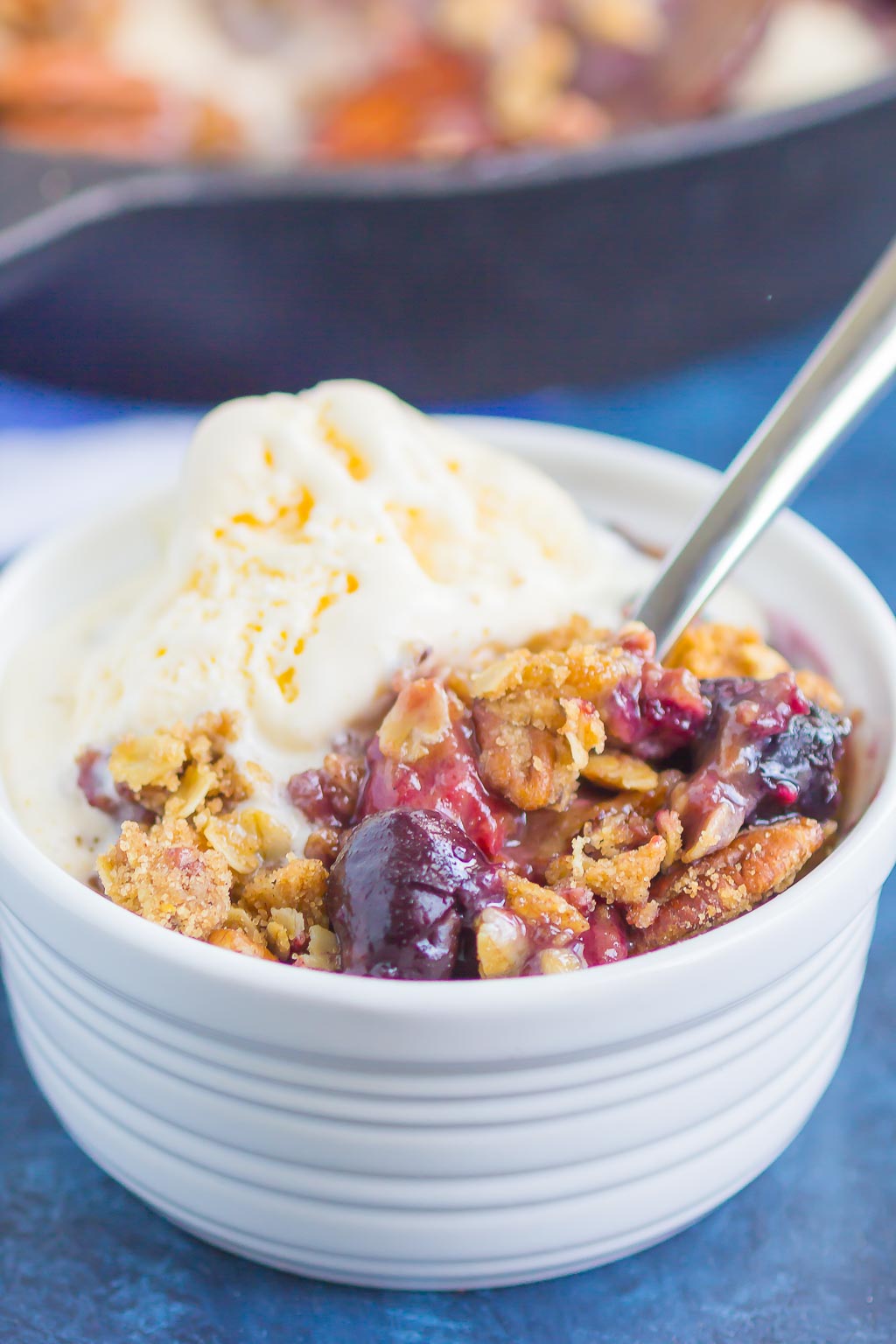 A serving of fruit crisp in a white bowl, topped with vanilla ice cream. 