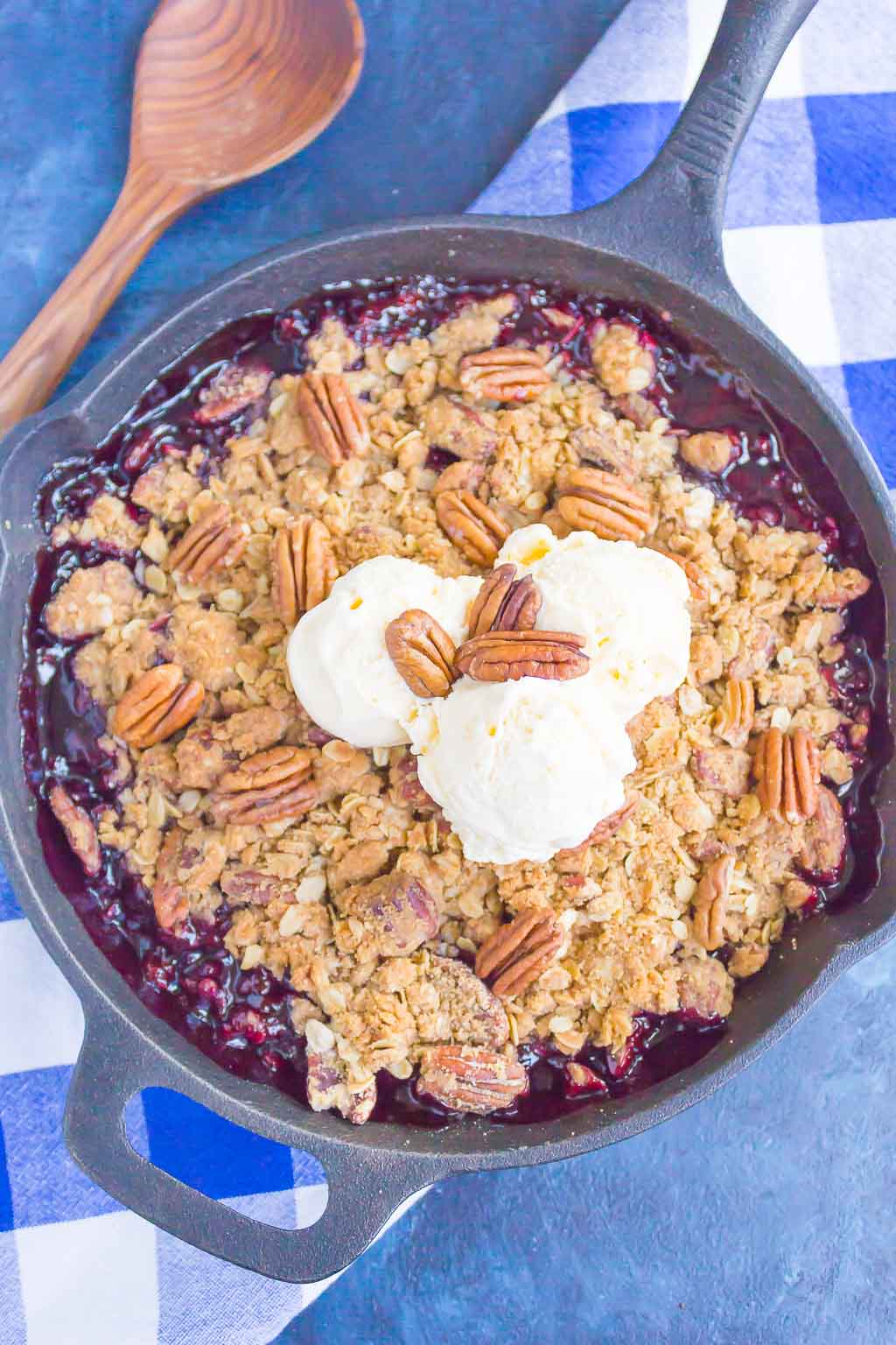 Overhead view of a cast iron skillet of cherry crisp topped with a pecan streusel and vanilla ice cream. 