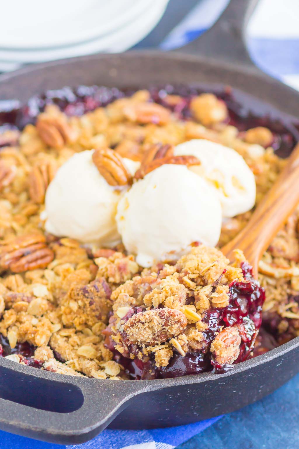 A fresh cherry crisp in a cast iron skillet, topped with three scoops of ice cream. 