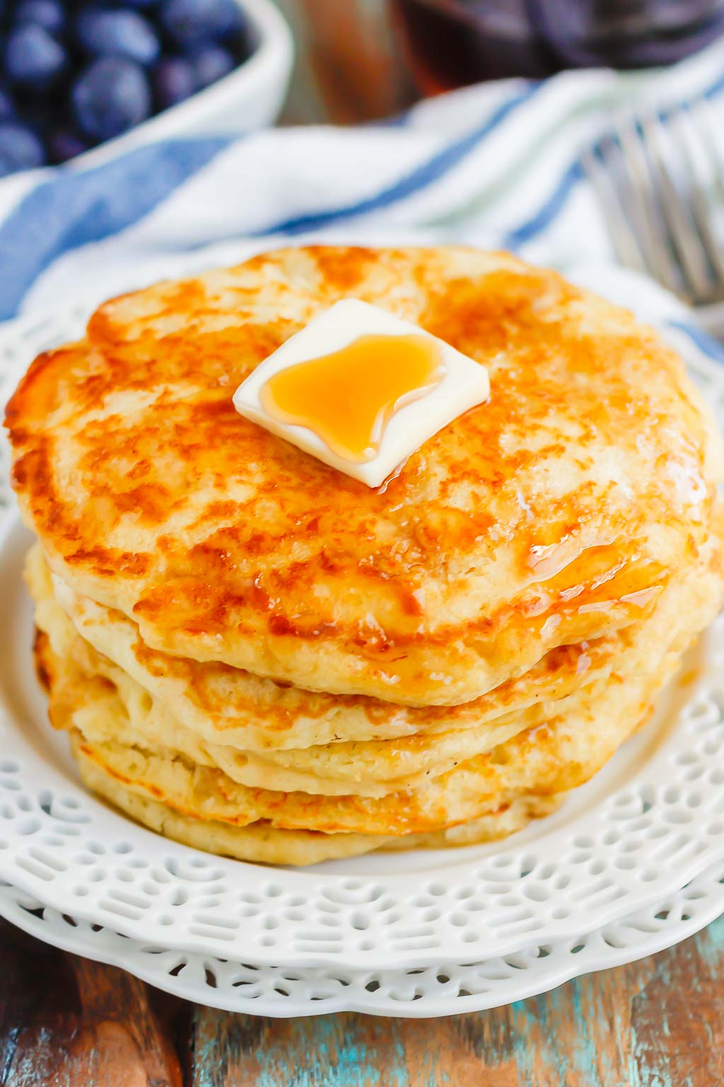 stack of four homemade buttermilk pancakes topped with butter and maple syrup on white plate