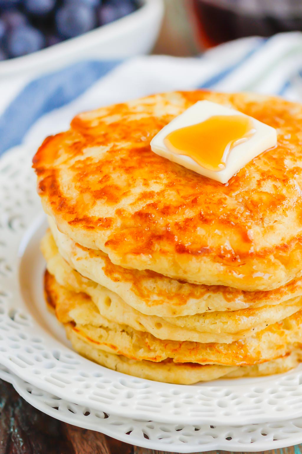 stack of buttermilk pancakes topped with syrup and butter on white plate