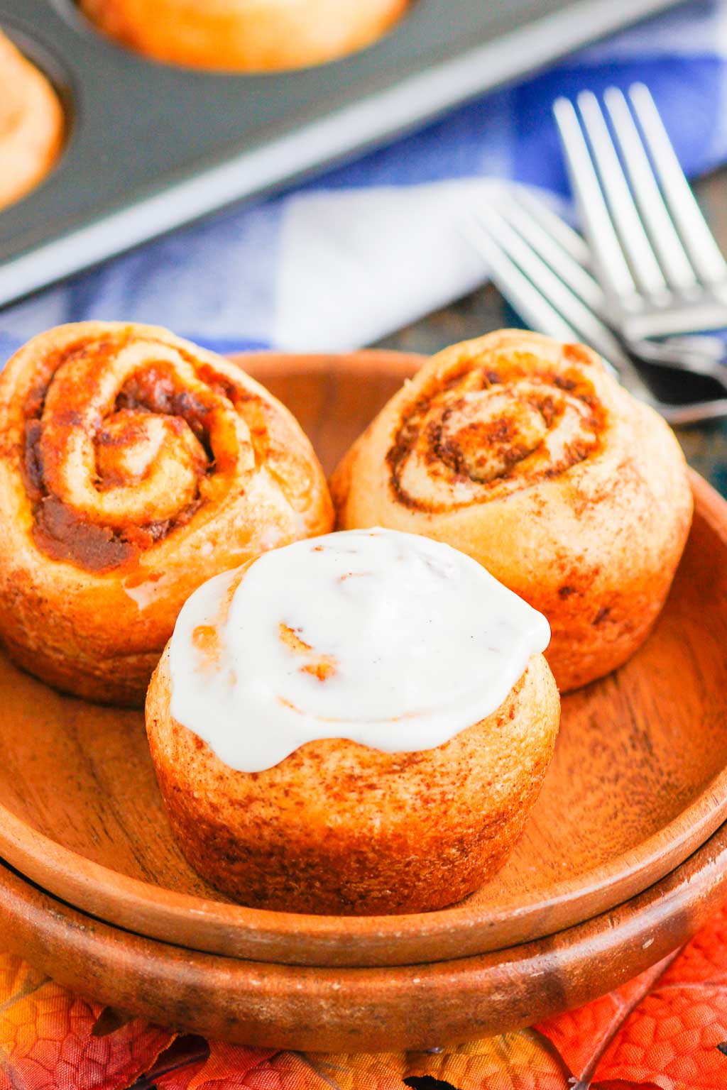 Three pumpkin cinnamon rolls made with crescent dough on a wood plate. 