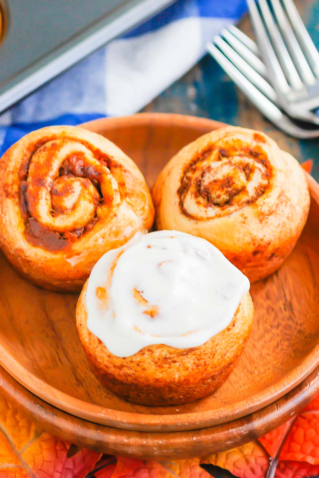 Three pumpkin spice cinnamon rolls made with crescent dough on a wood plate. 
