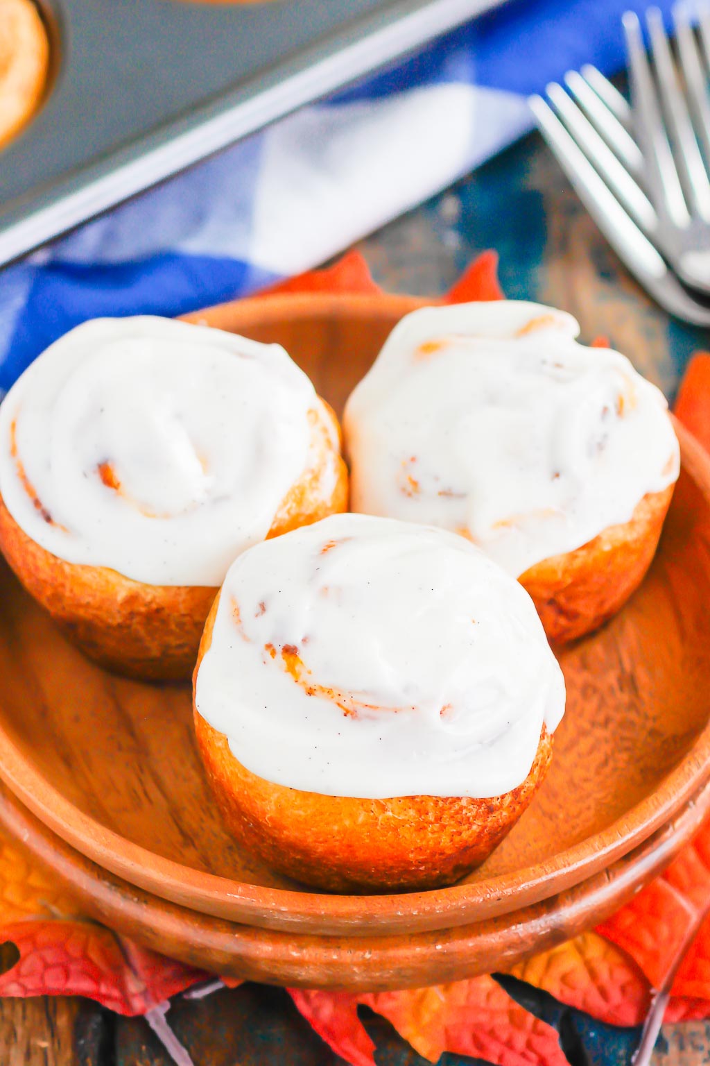 Three pumpkin cinnamon rolls made with crescent dough on a wood plate. 