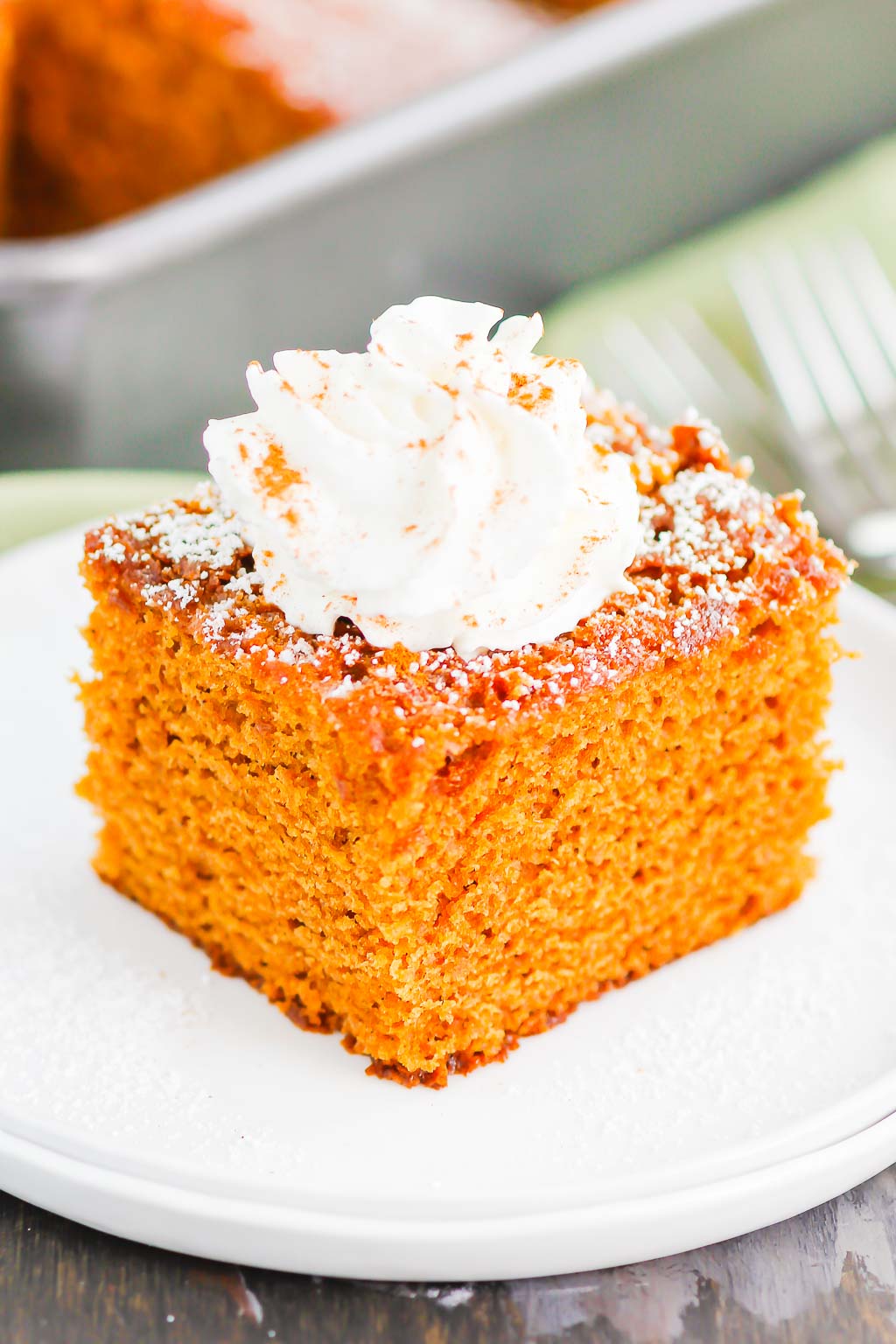 a slice of christmas gingerbread cake topped with whipped cream on a white plate. 