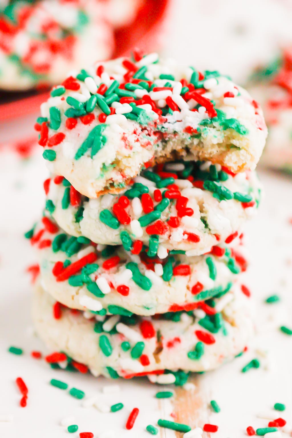 a stack of four sprinkle cookies. the top cookie is missing a bite. 