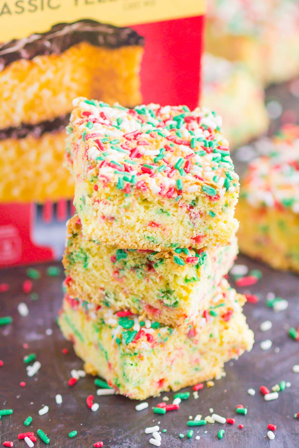 Stack of three yellow cake mix cookie bars in front of a box of cake mix. 