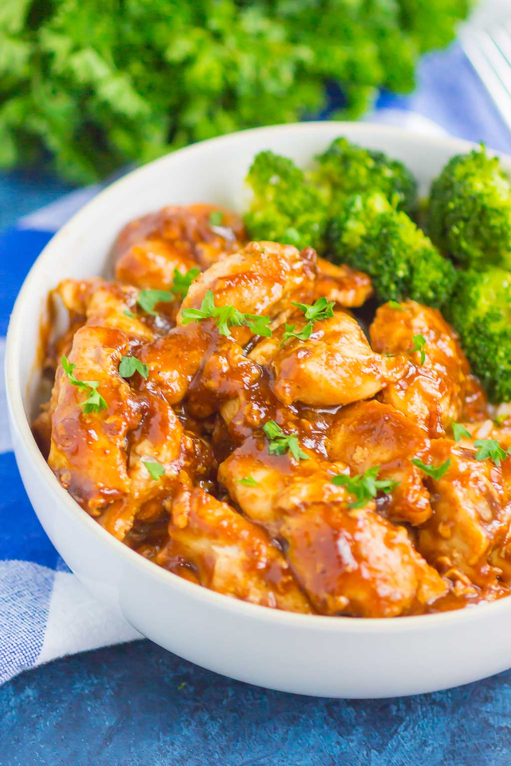 A white bowl with chicken coated in homemade teriyaki sauce and a side of broccoli. 