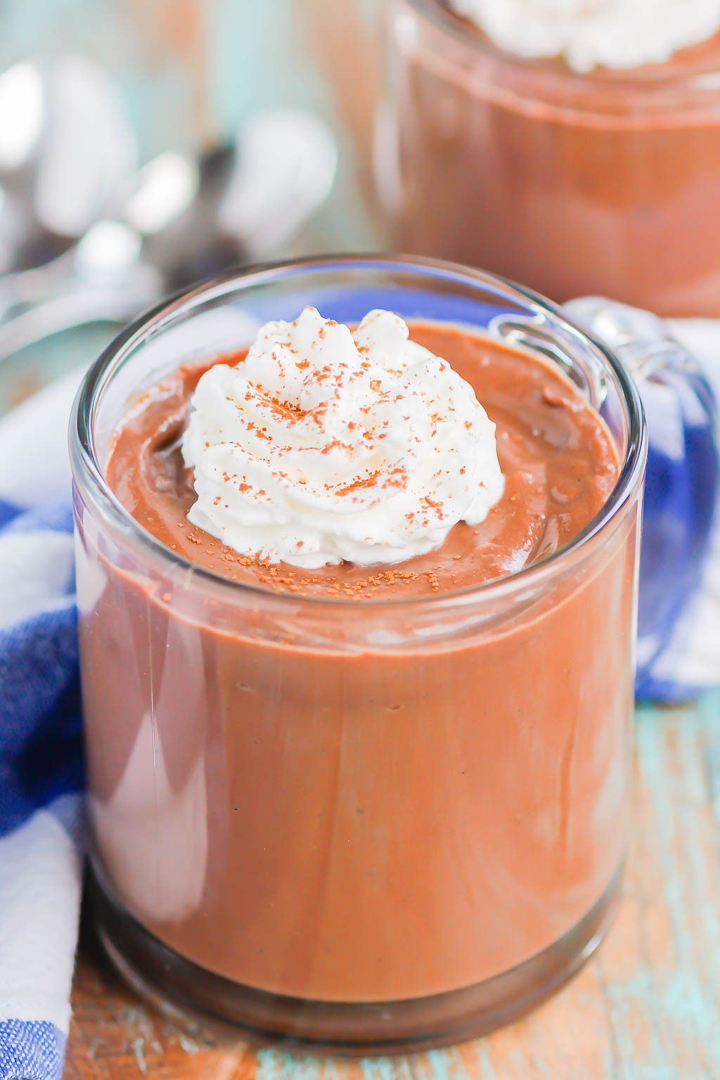 A glass mug filled with chocolate pudding from scratch and topped with whipped cream. 