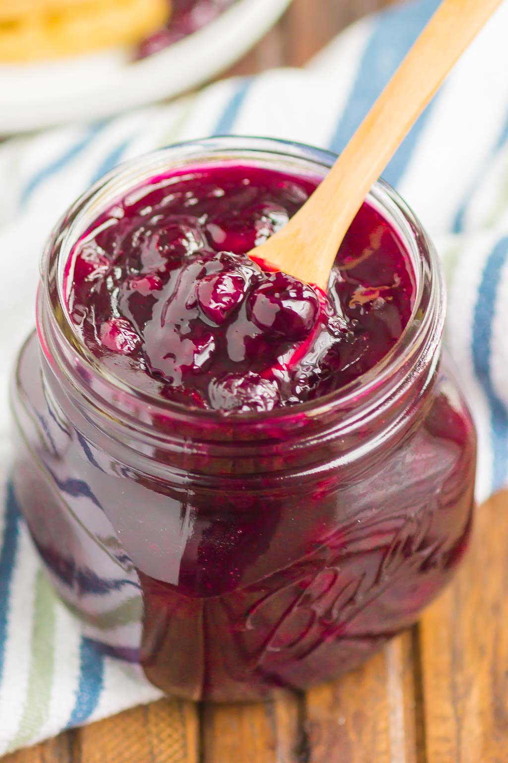 Homemade blueberry sauce in a small ball jar with a wooden spoon sticking out. 