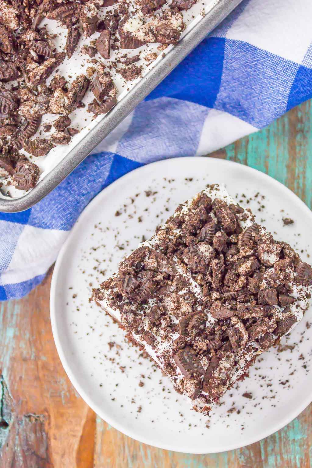 Overhead view of a slice of Oreo pudding poke cake on a dessert plate, next to a pan of cake. 