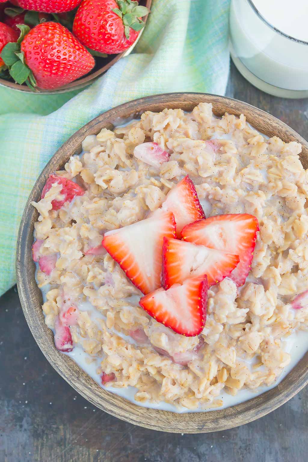 A bowl of strawberry oatmeal, viewed from above. A dish of strawberries rests beside it.  